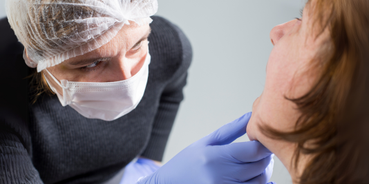 Clinician in PPE hold chin of a mature women and peers inside her mouth