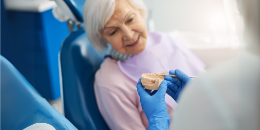 Mature woman in dental chair views a dental model held by a clinician in blue gloves