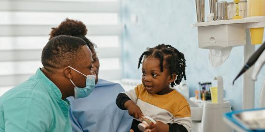 Child on mother's lap interacting with oral health professional in dental office