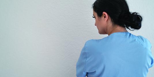 Woman in scrubs standing with arms crossed facing a wall