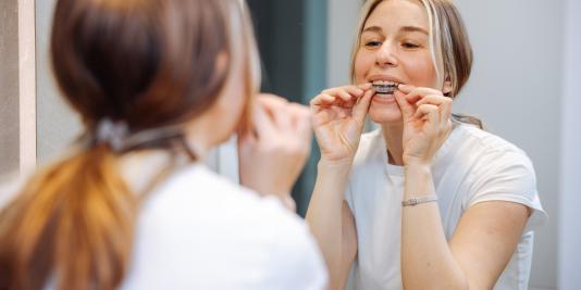 Young woman viewing mirror as she fits a device over her teeth herself